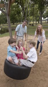 Siblings Fraiser, left, Evie Jane and Carter Johnston swing as parents Brian and Laura Beth Johnston look on. UMMC photo